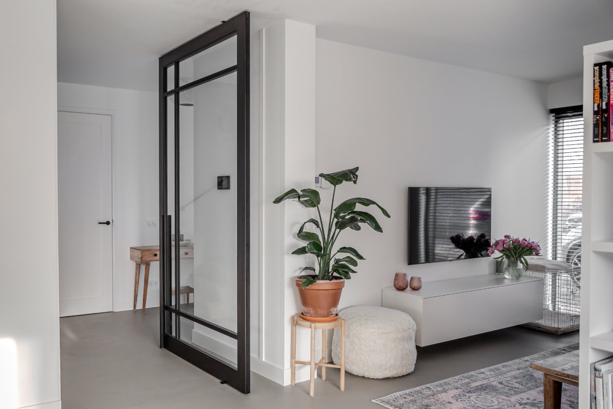 Zwarte taatsdeur open in een witte woonkamer met plant