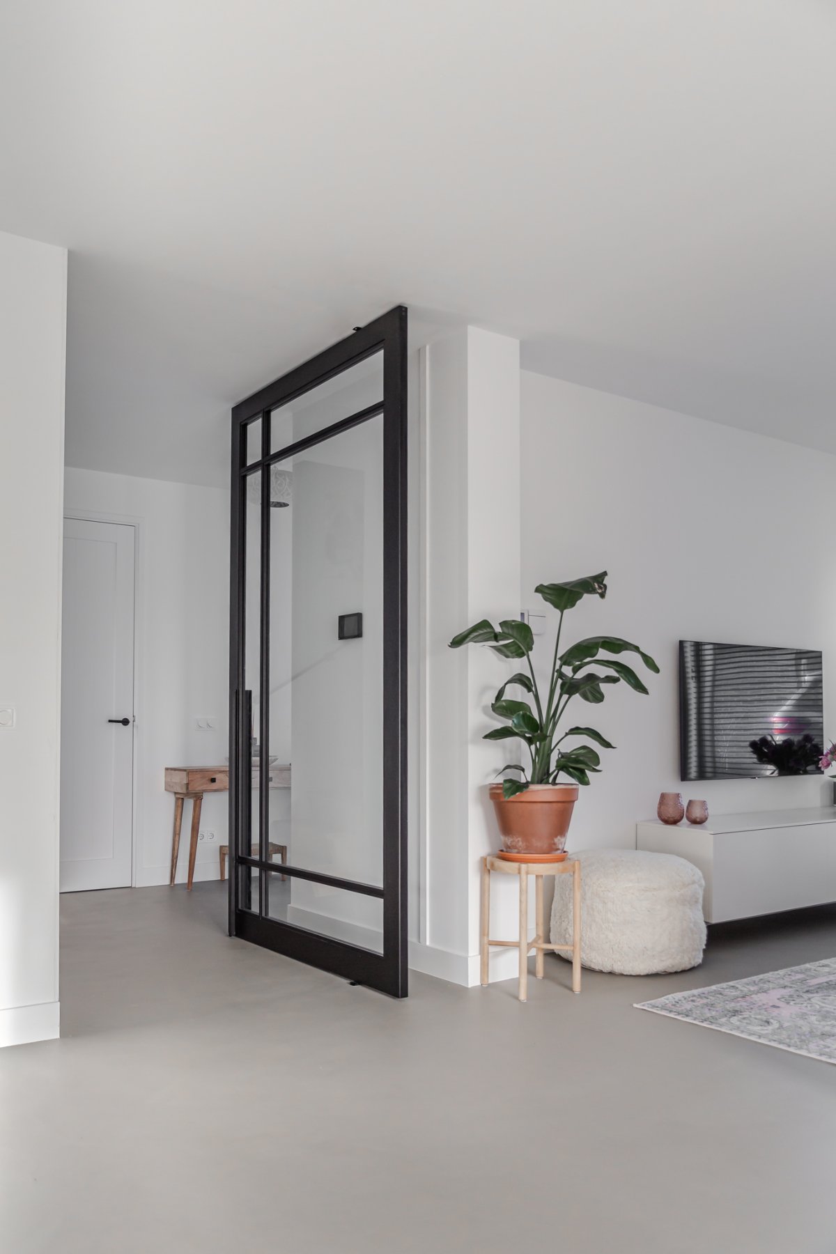 Zwarte stalen taatsdeur, half geopend in een witte woonkamer