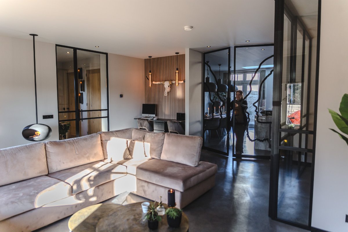 Stalen glaswand met deur tussen woonkamer en hal, betonvloer en warm licht